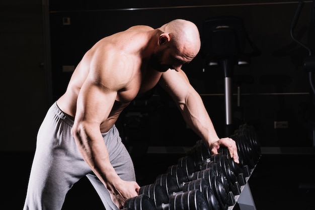 Free photo man taking dumbbell from rack