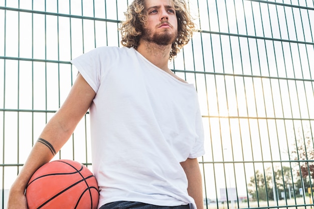 Foto gratuita uomo con pallacanestro in piedi davanti al recinto