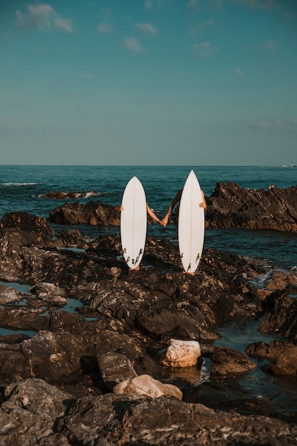 Foto gratuita l'uomo e la donna con tavole da surf si tengono per mano sulla costa rocciosa