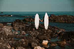 Foto gratuita l'uomo e la donna con tavole da surf si tengono per mano sulla costa di pietra