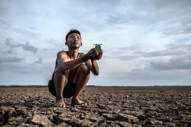 Free photo men sit in their hands, holding seedlings on dry ground and looking at the sky.