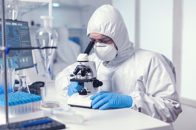 Free photo microbiologist with protection glasses using microscope dressed ppe suit