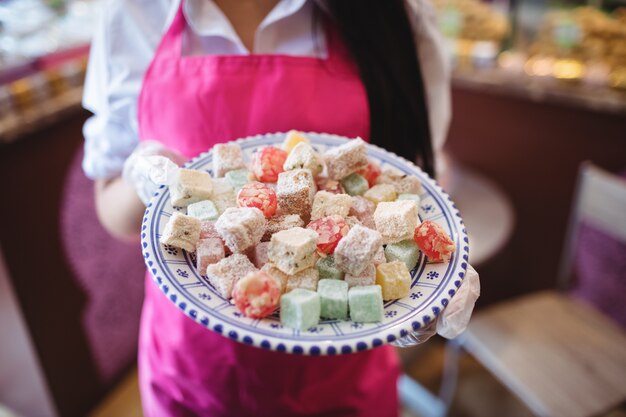 Free photo mid section of female shopkeeper holding tray of turkish sweets at counter