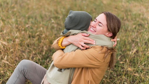 Free photo mom hugging her son while sitting on grass