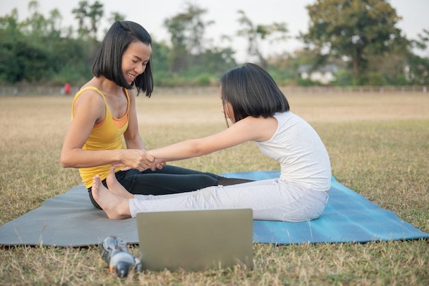 Free photo mother and daughter doing yoga. woman and child training in the park. outdoor sports. healthy sport lifestyle,watching yoga exercises online video tutorial and seated forward bend pose.