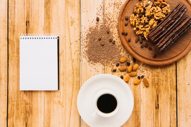 Notepad and cup of coffee near nuts on cutting board