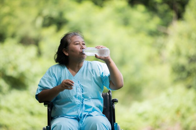 Old woman sit on wheelchair with water bottle after take a medicine