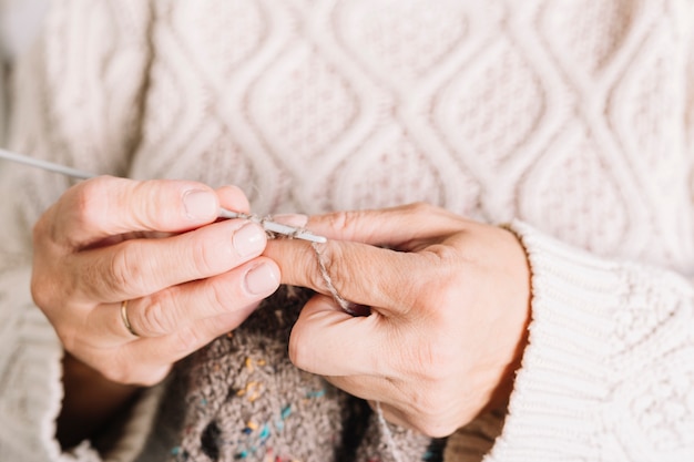 Old woman in sweater knitting scarf