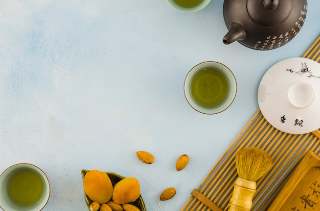 Free photo an overhead view of dried fruits; tea cups and teapot on textured backdrop