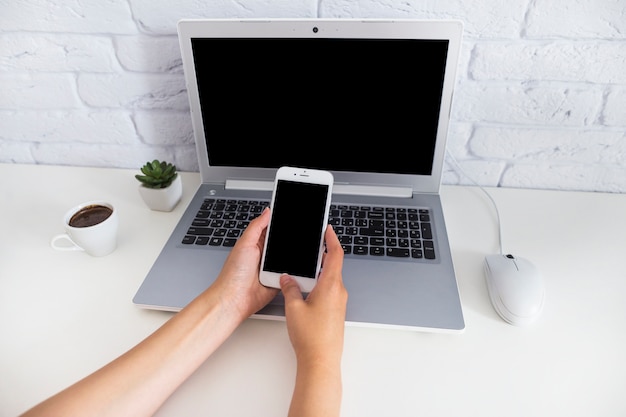 Free photo overhead view of hand holding smartphone over the laptop