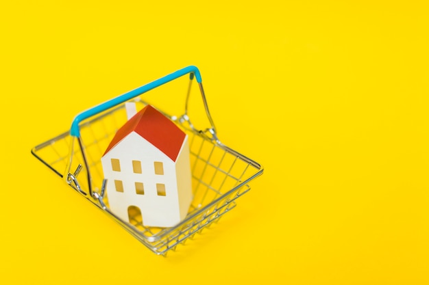 Free photo an overhead view of house model inside the shopping cart against yellow background