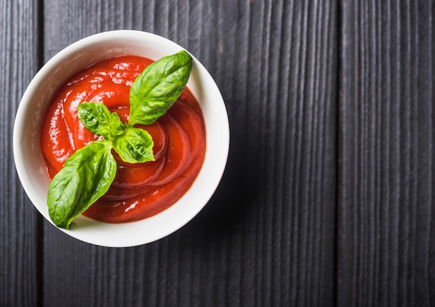 Free photo an overhead view of tomato sauce with green basil leaves on wooden backdrop