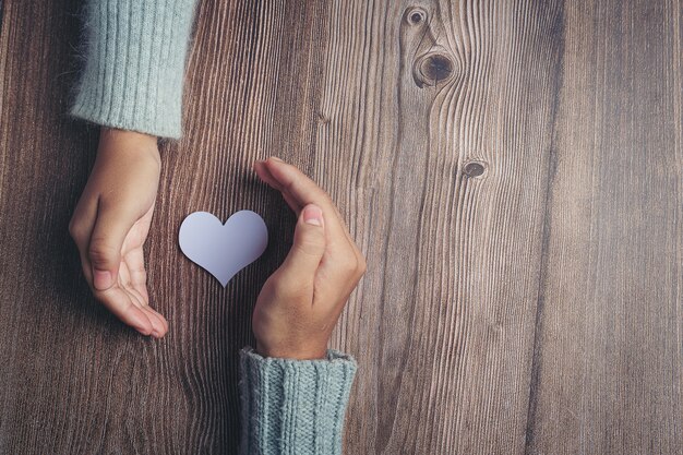 Paper heart and couple's hands on wooden table