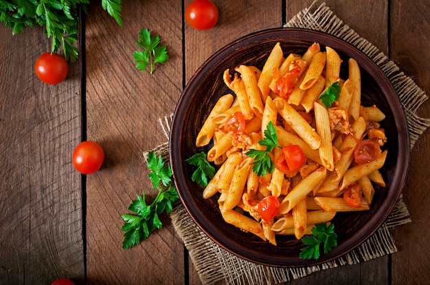 Free photo penne pasta in tomato sauce with chicken and tomatoes  on a wooden table