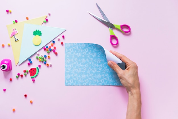 Free Photo a person hand holding folding blue paper over the pink background