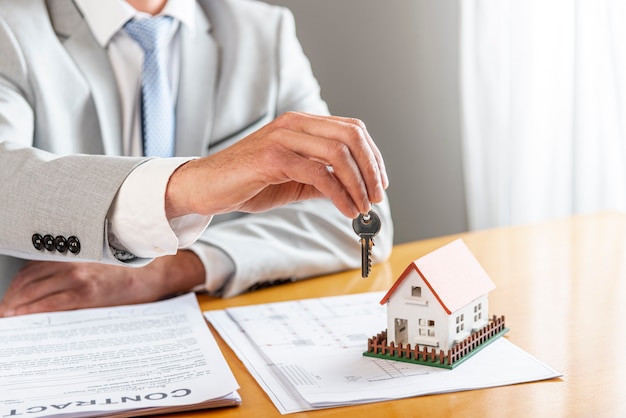 Free photo person holding house keys and toy model house on desk