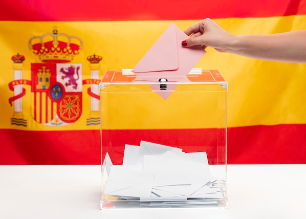 Person putting an envelope in a vote box and spanish flag background