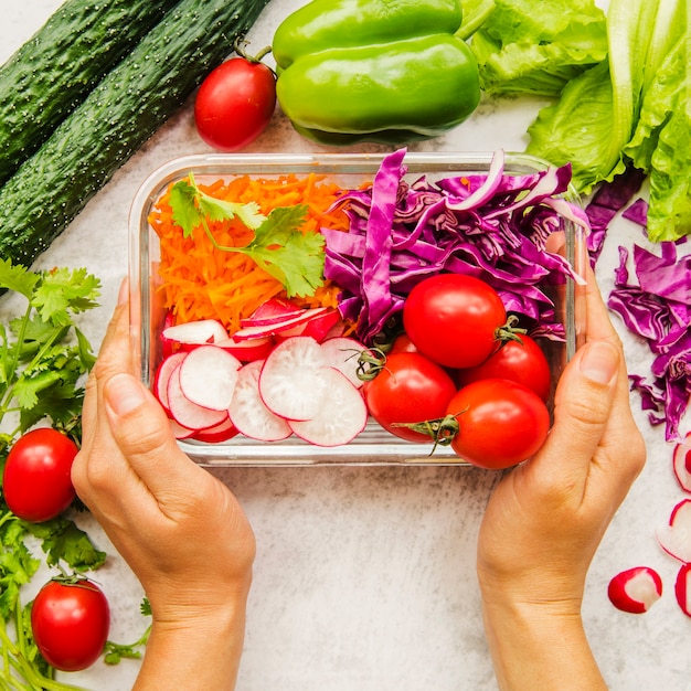 Person's hand holding fresh vegetables and ingredients for salad in container