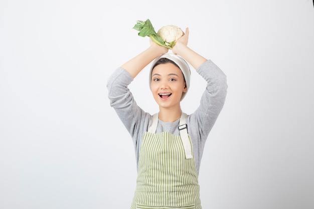 Free photo photo of a young nice woman model in apron holding a cauliflower overhead