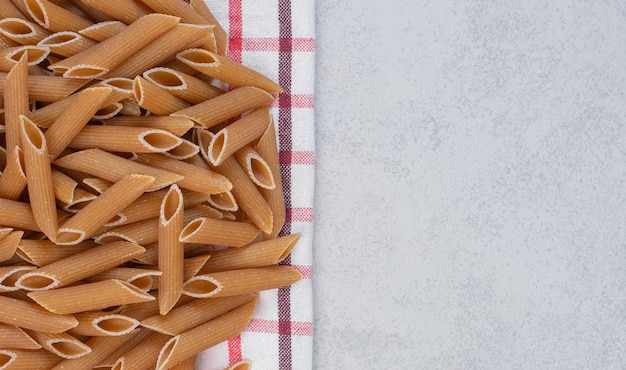 Free photo pile of dry penne pasta with tablecloth on stone.