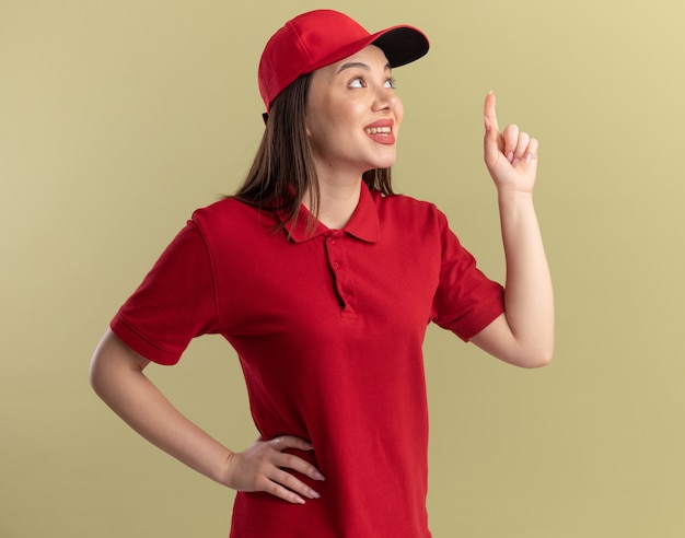 Free photo pleased pretty delivery woman in uniform looks and points up