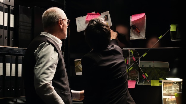 Free photo police agents examine evidence board in investigation office, analyzing unearthed clues to build case file. detectives team working with classified documents and records to catch suspect.