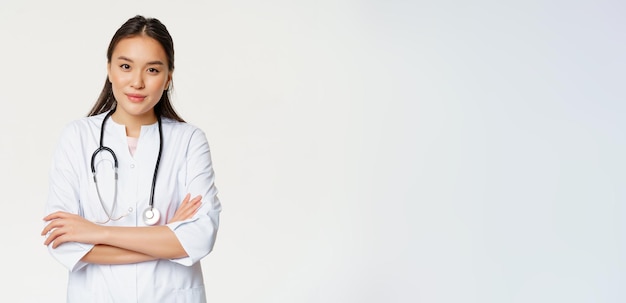 Foto gratuita ritratto di donna medico asiatico braccia incrociate in piedi in uniforme medica e stetoscopio sorridente in cam