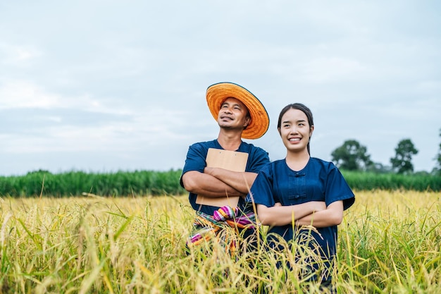 Free photo portrait asian middle aged man wearing straw hat and loincloth and young woman farmer stand and cross arms in rice field together