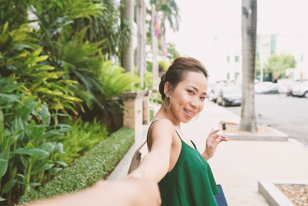 Free photo portrait of asian woman turning back and looking at camera pulling hand of her unrecognizable boyfriend