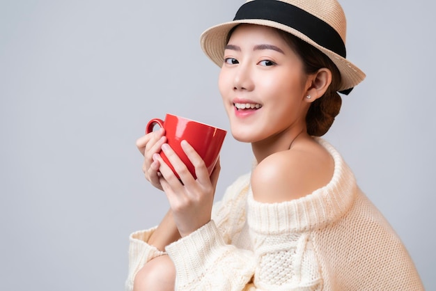 Free Photo portrait of beautiful asian female in summer travel dress hand hold red ceramic cup of hot drinh with smile and cheerful white background