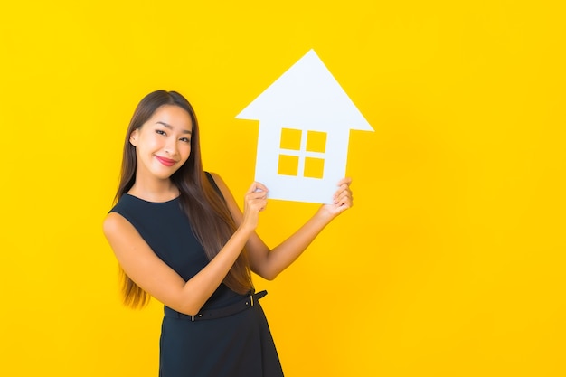 Free photo portrait beautiful young asian business woman with house paper sign board on yellow background