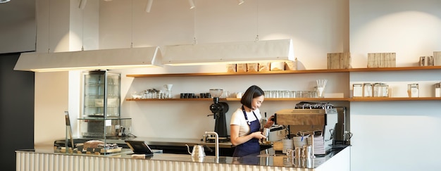 Free photo portrait of cafe counter with barista girl working with coffee machine making order for client in