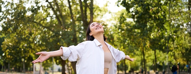 Free photo portrait of carefree young asian woman dancing in park alone enjoying freedom smiling with joy