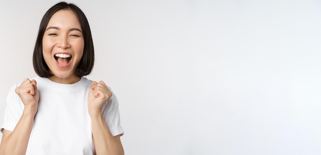 Free photo portrait of enthusiastic asian woman winning celebrating and triumphing raising hands up achieve goa