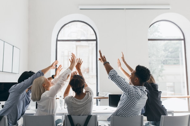 Free Photo portrait from back of tired students stretching after long work. indoor photo of office workers fooling around during meeting in conference hall with big windows.