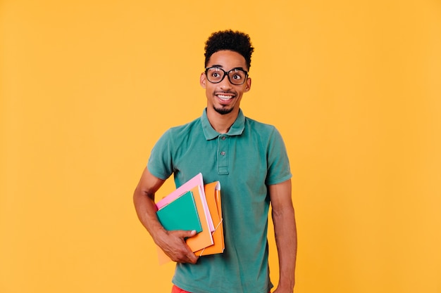 Free Photo portrait of funny african student in green t-shirt. photo of blissful black boy in glasses holding books and textbooks after exams.