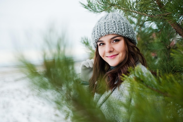 Free photo portrait of gentle girl in gray coat and hat against new year tree outdoor