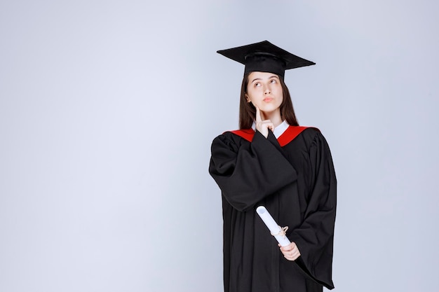 Free photo portrait of graduate student in gown holding diploma and standing. high quality photo