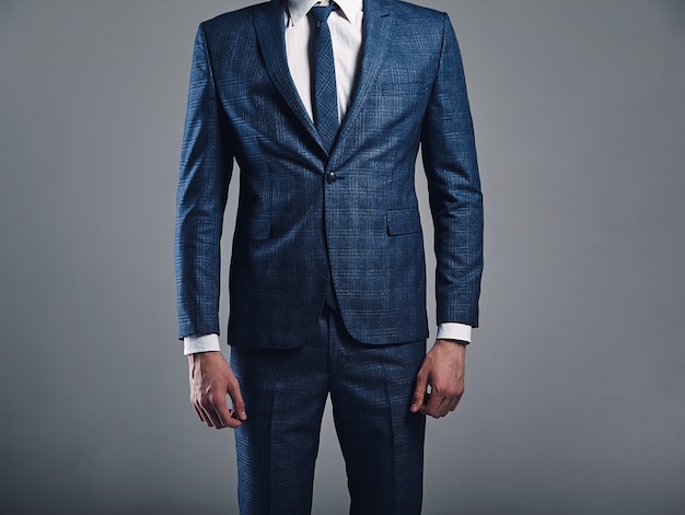 Foto gratuita il ritratto di bello modello alla moda dell'uomo d'affari si è vestito in vestito blu elegante che posa sul fondo grigio in studio