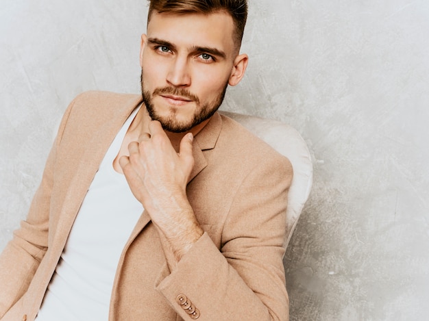 Free photo portrait of handsome smiling hipster   businessman model wearing casual beige suit. sitting in chair in interior