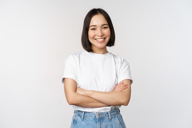 Free photo portrait of happy asian woman smiling posing confident cross arms on chest standing against studio background