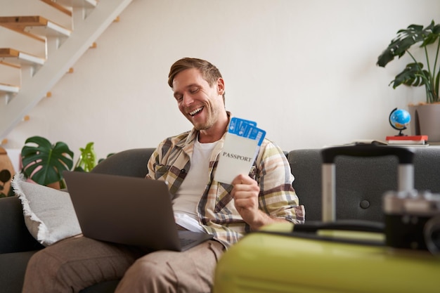 Free photo portrait of happy tourist man looking excited at laptop screen holding flight tickets going on