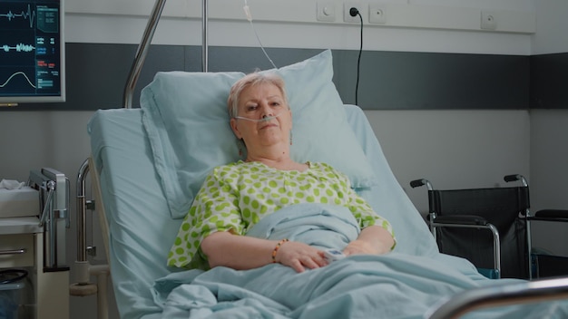 Free photo portrait of pensioner waiting to receive medical support in hospital ward, laying in bed with nasal oxygen tube and iv drip bag. aged patient preparing to cure sickness. healthcare service