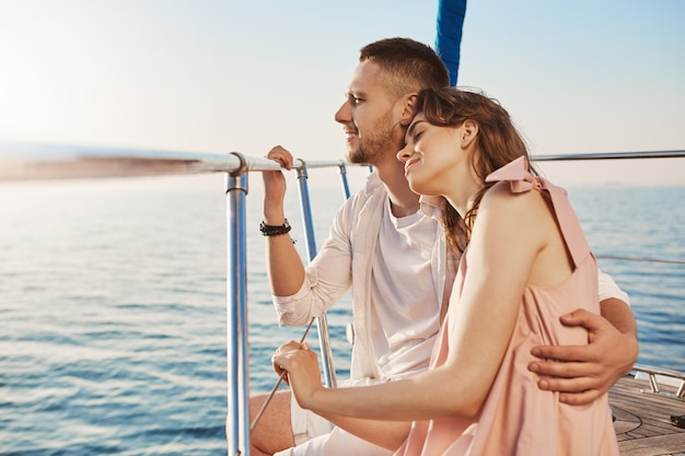 Foto gratuita ritratto delle coppie alla moda nell'amore, abbracciando mentre sedendosi sulla prua dell'yacht privato e godendo della vista del mare. il marito ha portato sua moglie in un bellissimo paese caldo, celebrando la luna di miele