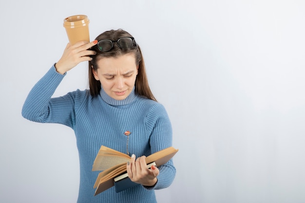 Portrait of a woman in eyeglasses reading a book with a cup of coffee.