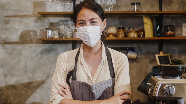 Free photo portrait young asian girl waitress wear medical face mask feeling happy smile waiting for clients after lockdown at urban cafe.