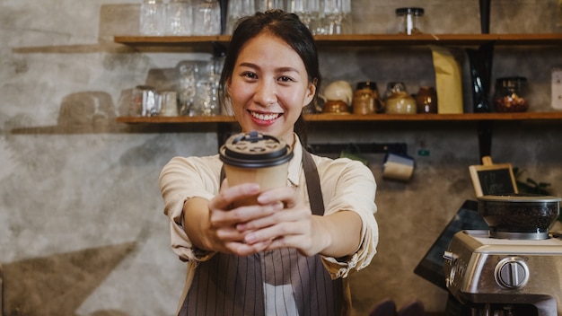 Free photo portrait young asian lady barista waitress holding coffee cup feeling happy at urban cafe.