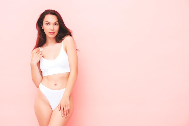 Free photo portrait of young beautiful smiling woman in white lingerie. sexy carefree cheerful model in underwear posing near pink wall in studio. positive and happy female enjoying morning