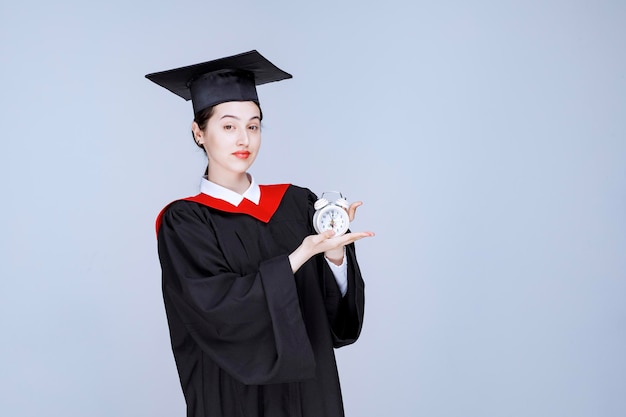 Free Photo portrait of young female graduate student holding clock to show time. high quality photo