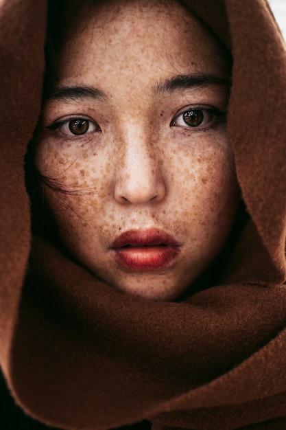 A portrait of a young Kazakh female with freckles covered in a brown blanket